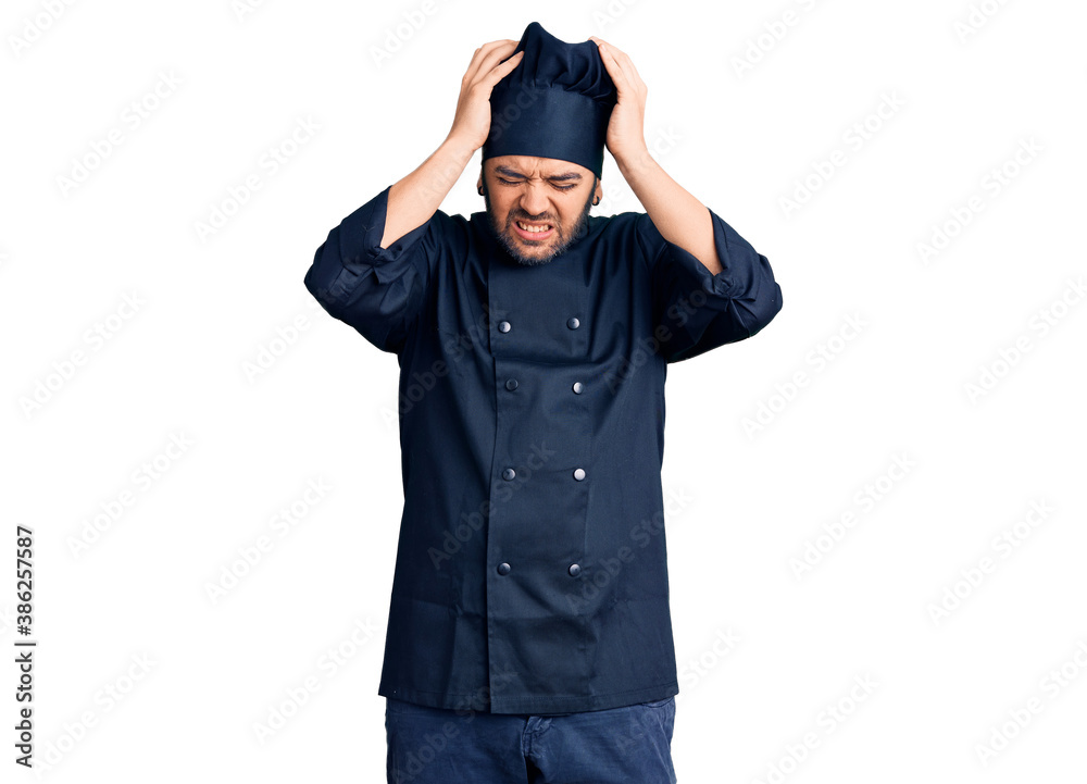 Young hispanic man wearing cooker uniform suffering from headache desperate and stressed because pain and migraine. hands on head. Young hispanic man wearing cooker uniform suffering from headache desperate and stressed because pain and migraine. hands on head.
