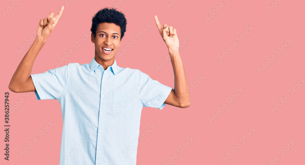 Young african american man wearing casual clothes smiling amazed and surprised and pointing up with fingers and raised arms. Young african american man wearing casual clothes smiling amazed and surprised and pointing up with fingers and raised arms.