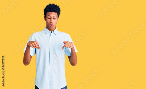Young african american man wearing casual clothes pointing down with fingers showing advertisement  surprised face and open mouth