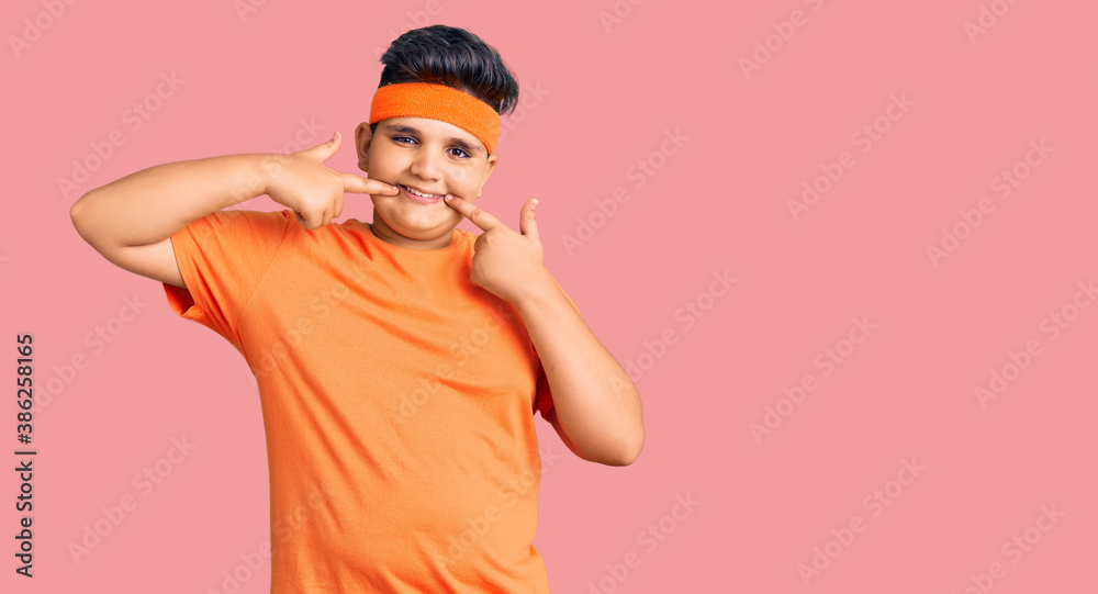 Little boy kid wearing sportswear smiling cheerful showing and pointing with fingers teeth and mouth. dental health concept. Little boy kid wearing sportswear smiling cheerful showing and pointing with fingers teeth and mouth. dental health concept.