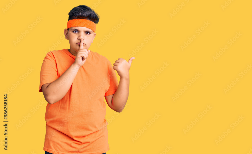 Little boy kid wearing sportswear asking to be quiet with finger on lips pointing with hand to the side. silence and secret concept.