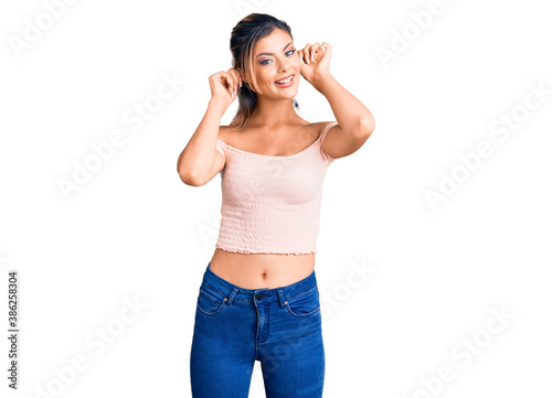 Young beautiful woman wearing casual clothes smiling pulling ears with fingers  funny gesture. audition problem