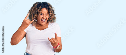 Young african american plus size woman wearing casual clothes shouting with crazy expression doing rock symbol with hands up. music star. heavy concept.