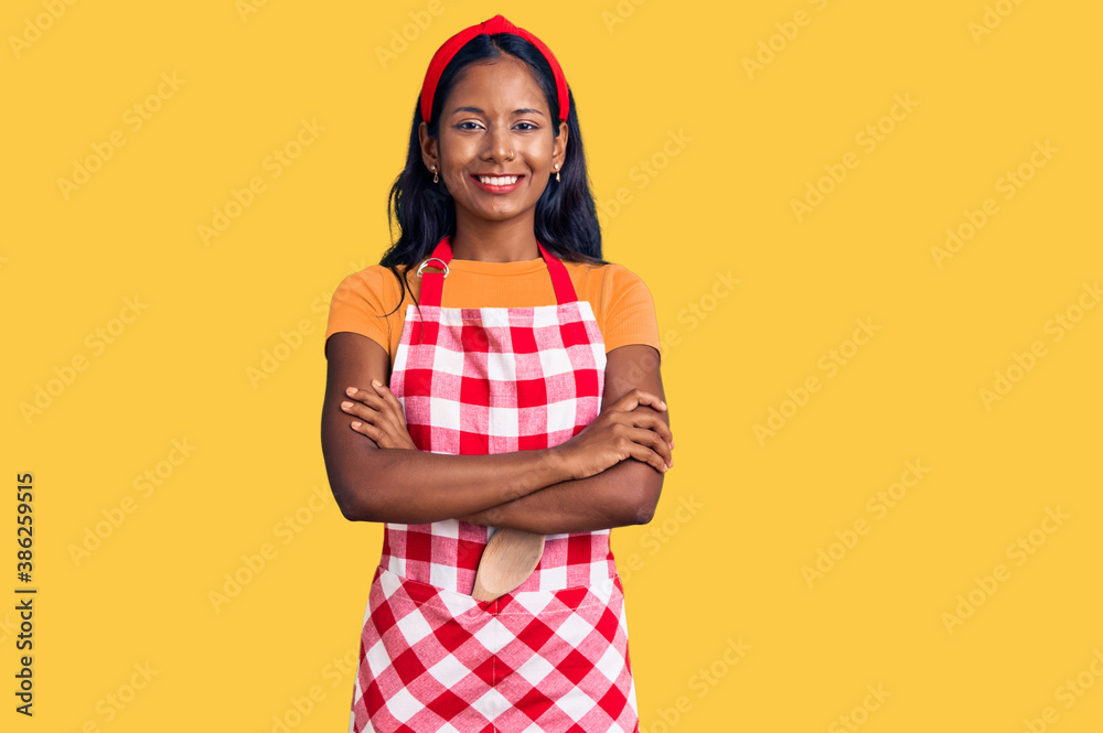 Young indian girl wearing professional baker apron happy face smiling with crossed arms looking at the camera. positive person. Young indian girl wearing professional baker apron happy face smiling with crossed arms looking at the camera. positive person.