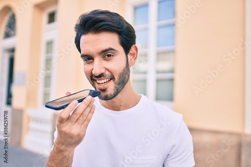 Young hispanic man smiling happy sending audio message using smartphone at city.