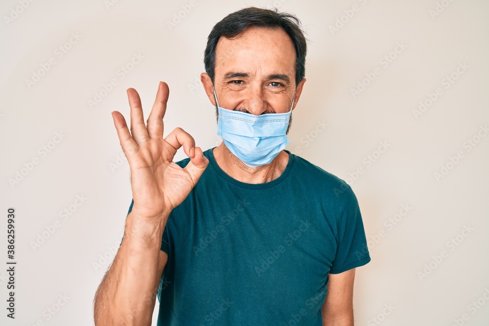 Middle age hispanic man wearing medical mask doing ok sign with fingers, smiling friendly gesturing excellent symbol Middle age hispanic man wearing medical mask doing ok sign with fingers, smiling friendly gesturing excellent symbol