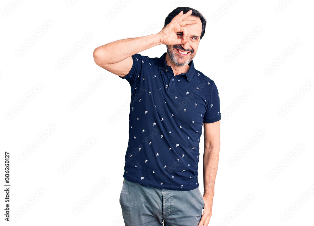 Middle age handsome man wearing casual polo smiling happy doing ok sign with hand on eye looking through fingers Middle age handsome man wearing casual polo smiling happy doing ok sign with hand on eye looking through fingers