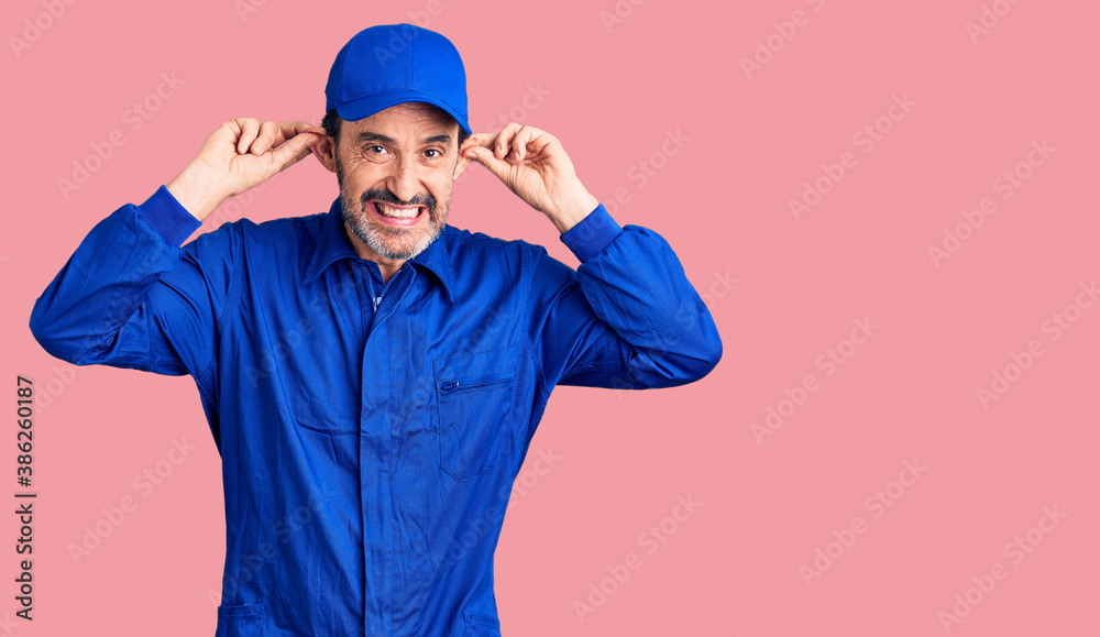 Middle age handsome man wearing mechanic uniform smiling pulling ears with fingers, funny gesture. audition problem Middle age handsome man wearing mechanic uniform smiling pulling ears with fingers, funny gesture. audition problem