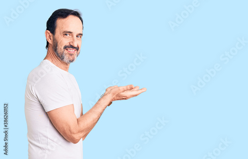 Middle age handsome man wearing casual t-shirt pointing aside with hands open palms showing copy space, presenting advertisement smiling excited happy