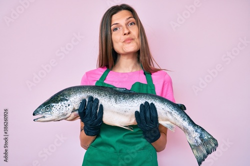 Beautiful caucasian woman fishmonger selling fresh raw salmon looking at the camera blowing a kiss being lovely and sexy. love expression.