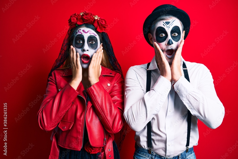 Couple wearing day of the dead costume over red afraid and shocked, surprise and amazed expression with hands on face Couple wearing day of the dead costume over red afraid and shocked, surprise and amazed expression with hands on face