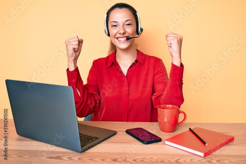 Young brunette woman wearing operator headset at the call center office screaming proud, celebrating victory and success very excited with raised arms photo