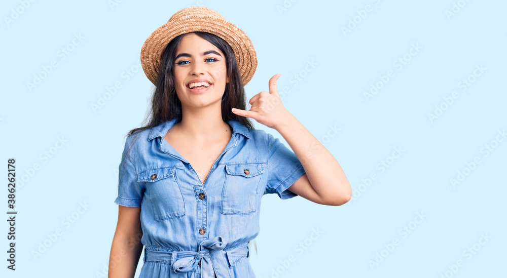 Brunette teenager girl wearing summer hat smiling doing phone gesture with hand and fingers like talking on the telephone. communicating concepts.
