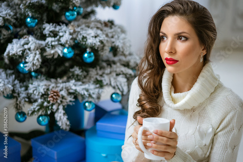 Beautiful young woman with a mug in her hand at the Christmas tree