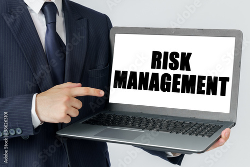 A businessman holds a laptop in his hands and shows on the screen with the text - RISK MANAGEMENT