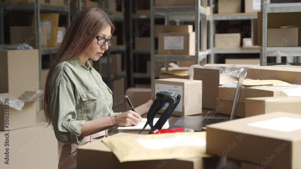 Female warehouse worker online store owner using laptop at work preparing parcel boxes checking ecommerce shipping online retail e commerce store order fulfillment in dropship delivery post office.
