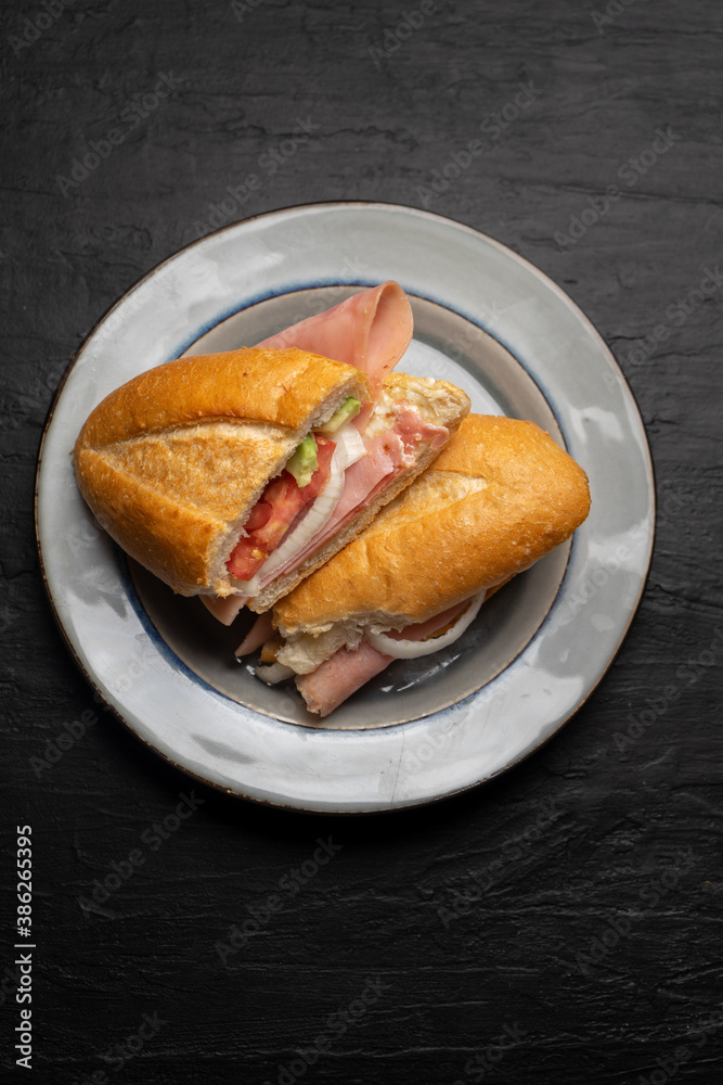 Mexican ham sandwich with avocado and cheese also called torta on dark background Mexican ham sandwich with avocado and cheese also called torta on dark background