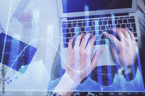 Double exposure of man's hands typing over laptop keyboard and forex chart hologram drawing. Top view. Financial markets concept.