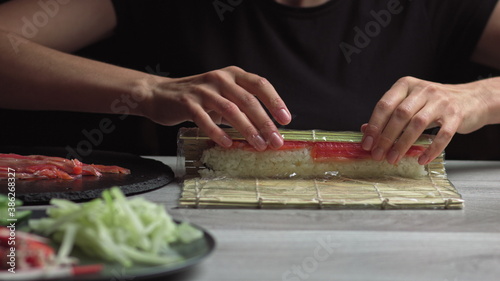 Japanese chef prepares sushi rolls with salmon and avocado. Cook hands making Japanese sushi roll on the bamboo mat. Delicious Japanese food, low-angle view