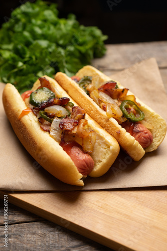 Hot dog with jalapeno pepper, bacon and caramelized onion on wooden background