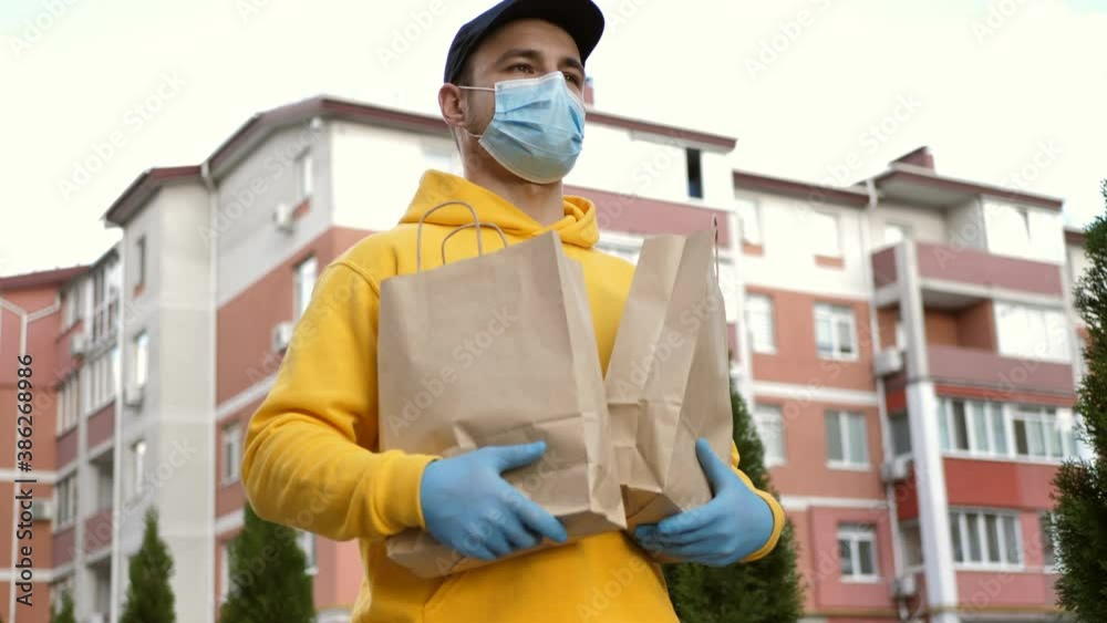 a young handsome guy, a courier in a peaked cap and a medical mask, walking down the street carries packages with delivery. male handsome courier will deliver online order