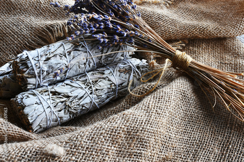An image of white sage smudge sticks and dried lavender flowers on vintage burlap cloth.  photo