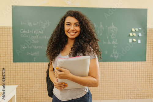 Billede på lærred Latin Curly haired student smiling wearing backpack holding a notebook in a clas