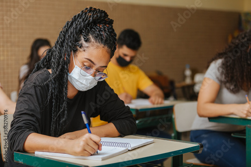 Latin students in the classroom. female student with twisted hair wearing mask and writing in notebook with a pen. Covid-19. Pandemic. photo