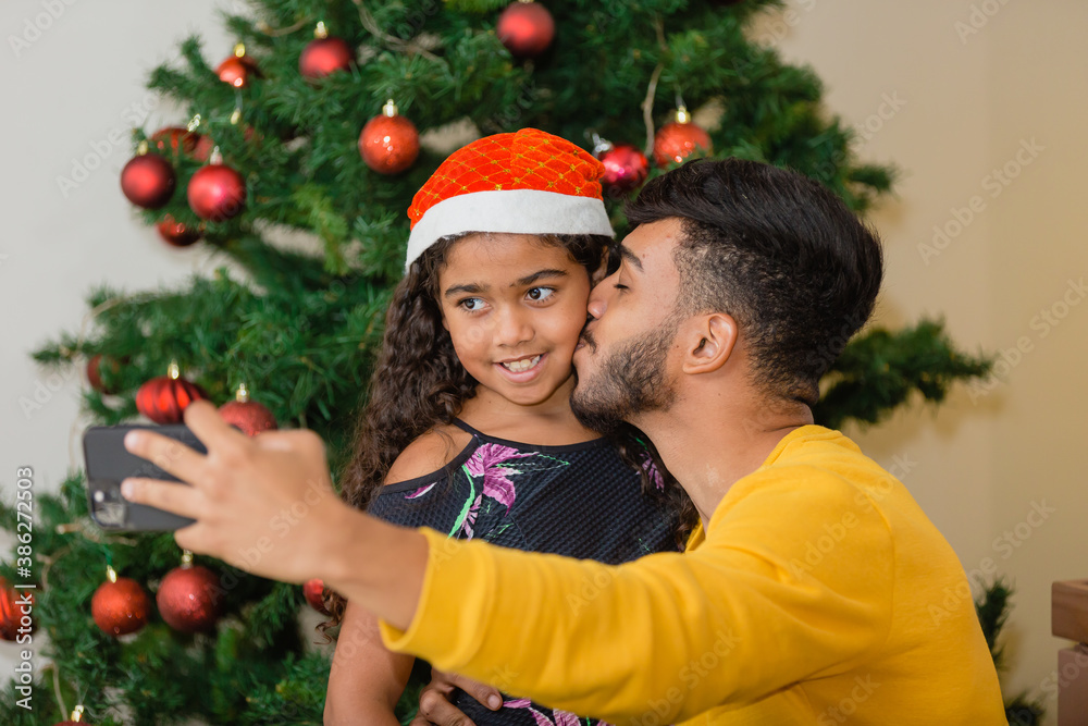 Summer Christmas dinner in Brazil. Real Brazilian family having fun at the Latin American Christmas party. father making a selfie giving a kiss to his daughter with curly hair Summer Christmas dinner in Brazil. Real Brazilian family having fun at the Latin American Christmas party. father making a selfie giving a kiss to his daughter with curly hair