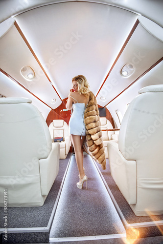 Beautiful rich woman in a dress and a fur coat in a private first class plane