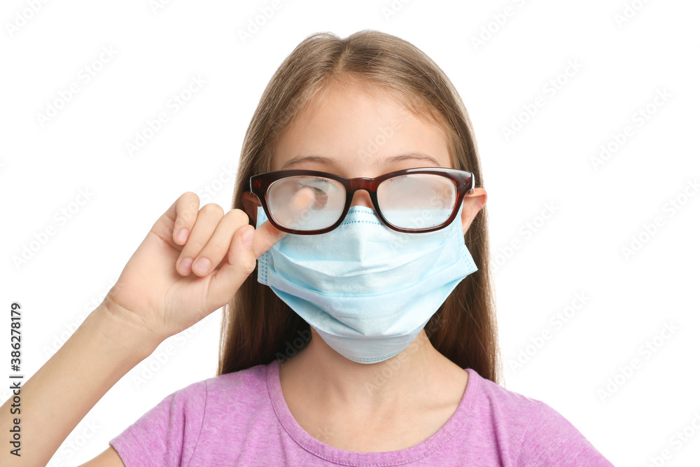 Little girl wiping foggy glasses caused by wearing disposable mask on white background. Protective measure during coronavirus pandemic