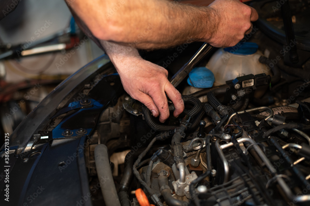 Senior Mechanic working on engine bay repairing a oil leak in home garage Senior Mechanic working on engine bay repairing a oil leak in home garage