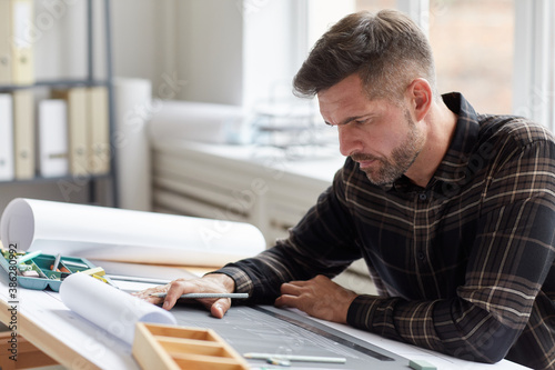 Portrait of mature bearded architect working on blueprints and plans while sitting at drawing desk in office, copy space