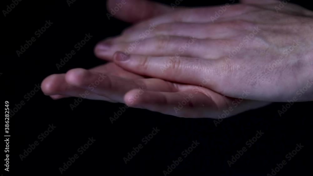 Person squeezing some hand sanitiser onto their hands and rubbing them together. Black background. Person squeezing some hand sanitiser onto their hands and rubbing them together. Black background.