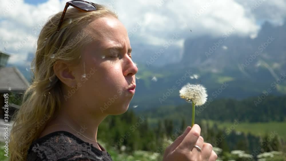 Blonde Female Model blowing a Dandelion flower in the wind the wrong way in the Val Gardena area, Dolomites Italy Blonde Female Model blowing a Dandelion flower in the wind the wrong way in the Val Gardena area, Dolomites Italy