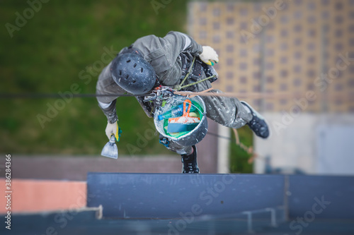 Professional climber rope access worker painting and repairing the facade of residential high rise building exterior facade wall, industrial mountaineer working at heights, risky job