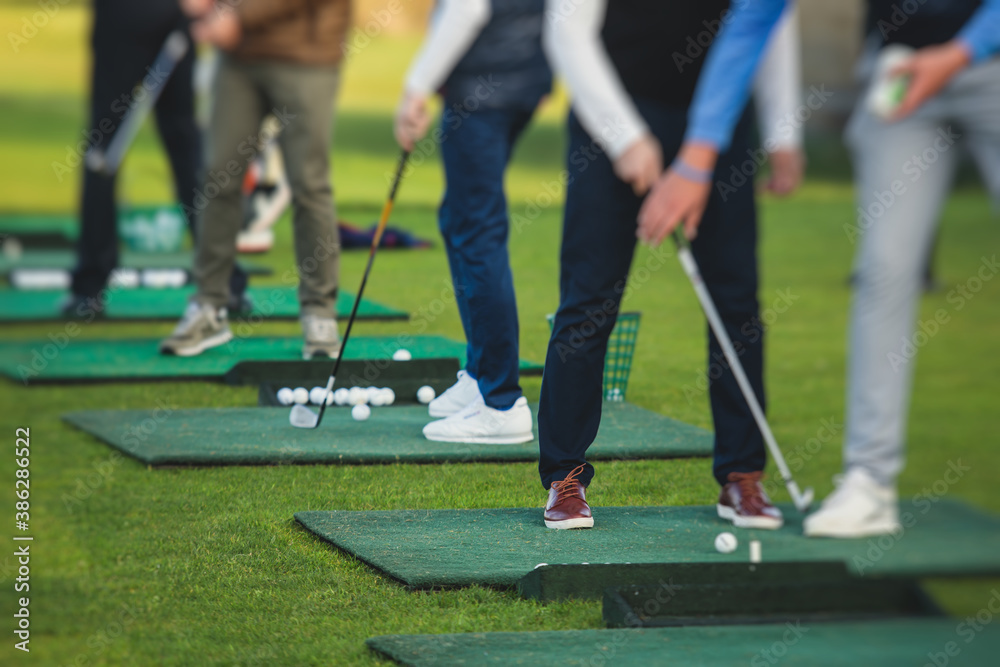 Obraz premium Group of golfers practicing and training golf swing on driving range practice, men playing on golf course, golf ball at golfing complex club resort