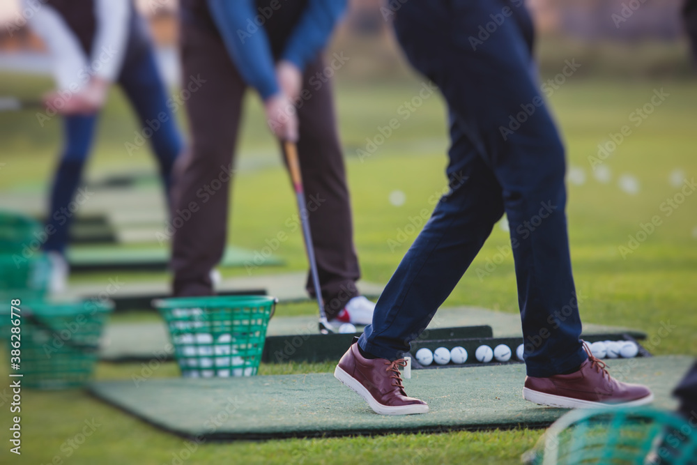 Obraz premium Group of golfers practicing and training golf swing on driving range practice, men playing on golf course, golf ball at golfing complex club resort