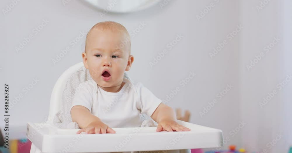 Portrait of young baby in white high baby chair. White walls on background. Portrait of young baby in white high baby chair. White walls on background.