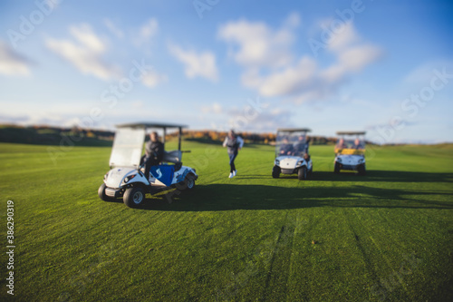 Golf electric cars riding on a golf course in the sunny day, golf carts drive with golfers in resort club