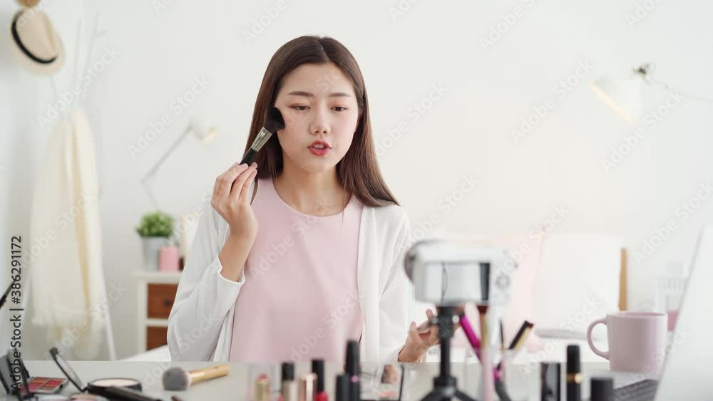 Young beautiful Asian woman professional beauty vlogger influencer recording make up tutorial video clip in bedroom at home for social media marketing