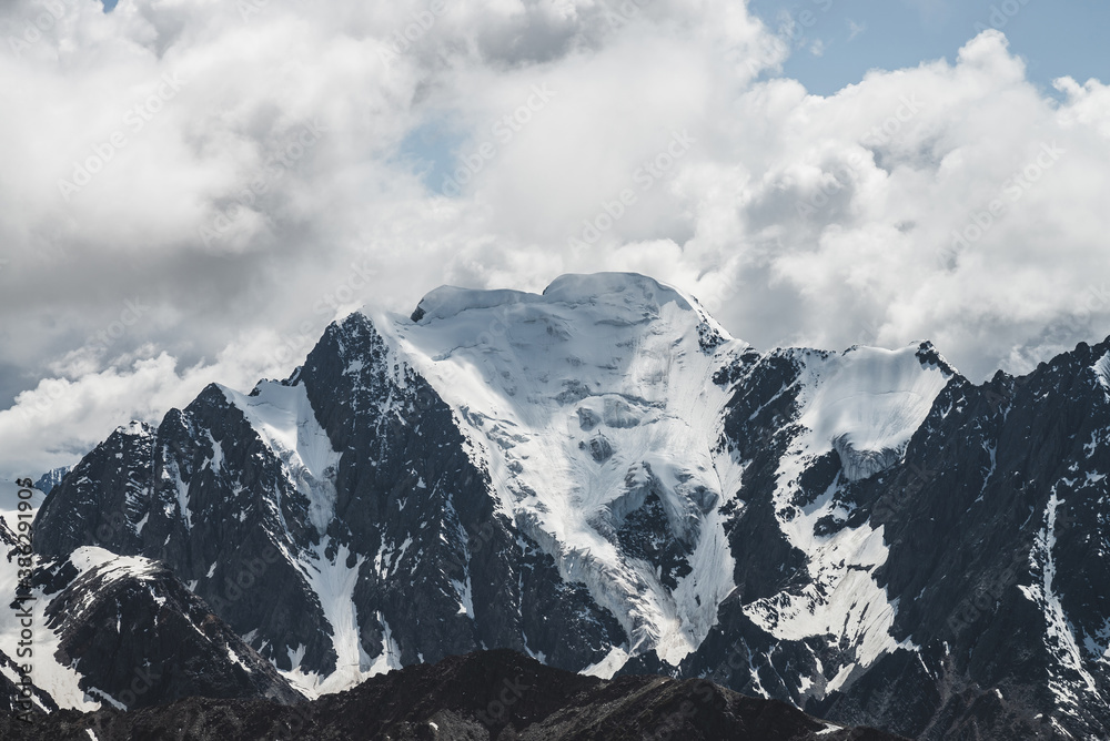 Atmospheric minimalist alpine landscape with massive hanging glacier on big mountain under cloudy sky. Cracks on ice. Low clouds over snowbound huge mountain range. Majestic scenery on high altitude.