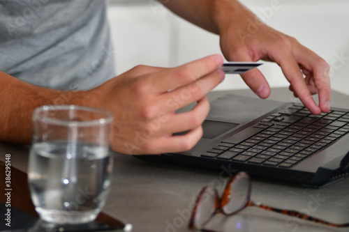 Close up of male hands holding a credit card while using a laptop on an out of focus background. Technology and online shopping concept.