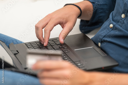 a man using a laptop while holding an out of focus credit card. Commerce and payment concept.