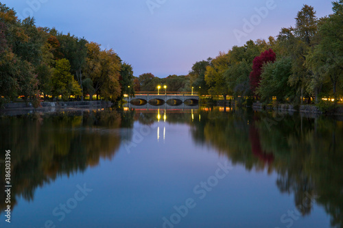 Autumn landscape. Evening time, colorful trees, slowly river. Mirror water and old stone bridge with lights . Guelph, Ontario, Canada