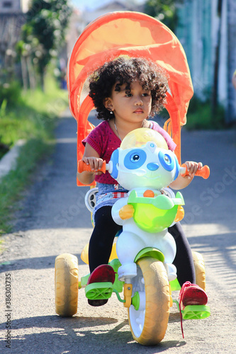 little child with curly hair playing with bicycle