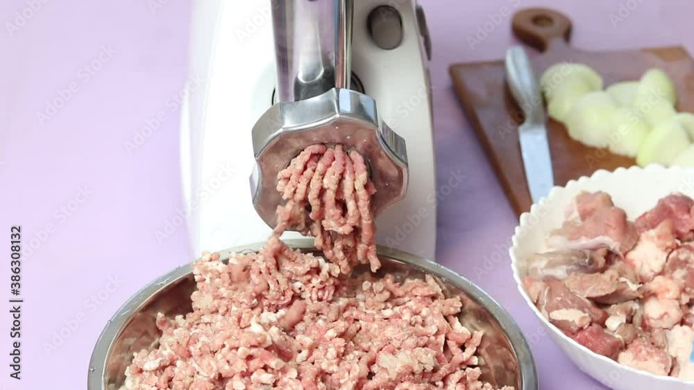 electric white meat grinder. She puts the minced meat in a metal bowl. A human hand in blue gloves straightens everything electric white meat grinder. She puts the minced meat in a metal bowl. A human hand in blue gloves straightens everything