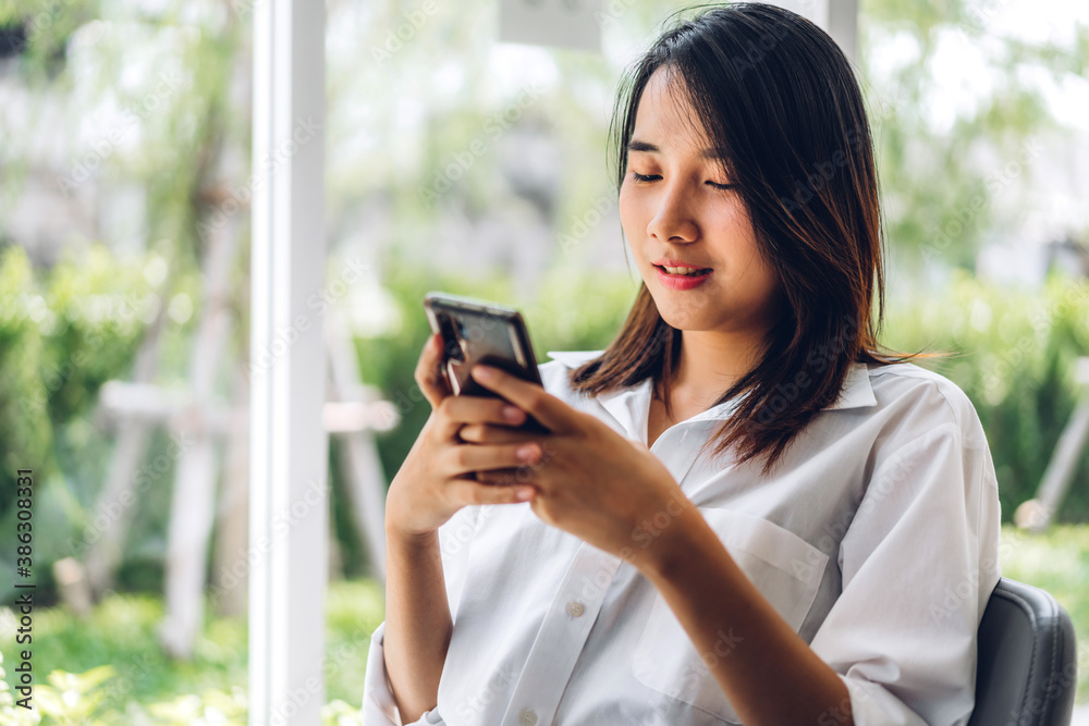 Portrait of smiling happy beautiful asian woman relaxing using digital smartphone.Young asian girl looking at screen typing message and playing game online or social media at cafe Portrait of smiling happy beautiful asian woman relaxing using digital smartphone.Young asian girl looking at screen typing message and playing game online or social media at cafe