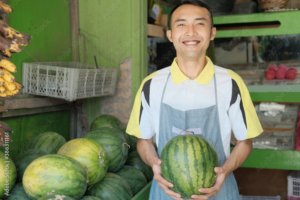 Fototapeta premium Shop waitress boy in apron carry watermelon at fruit stand, fresh fruit concept