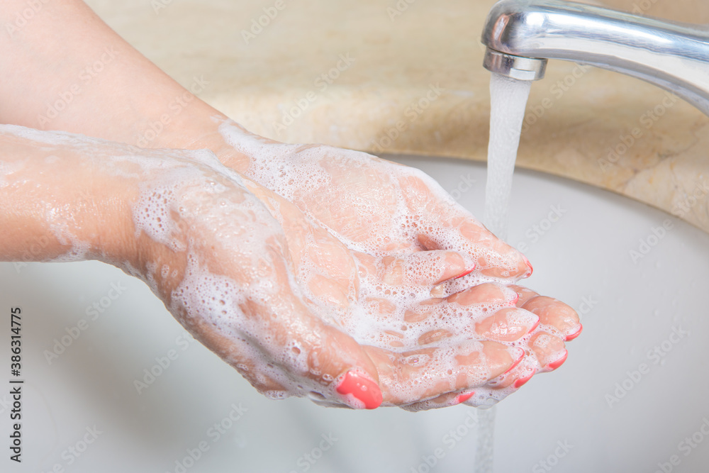 Fototapeta premium Woman Washing hands to prevent spread of CoronaVirus as well as cold, flu, bacteria at home. Woman use soap and washing hands under the water tap. Hygiene concept hand detail.